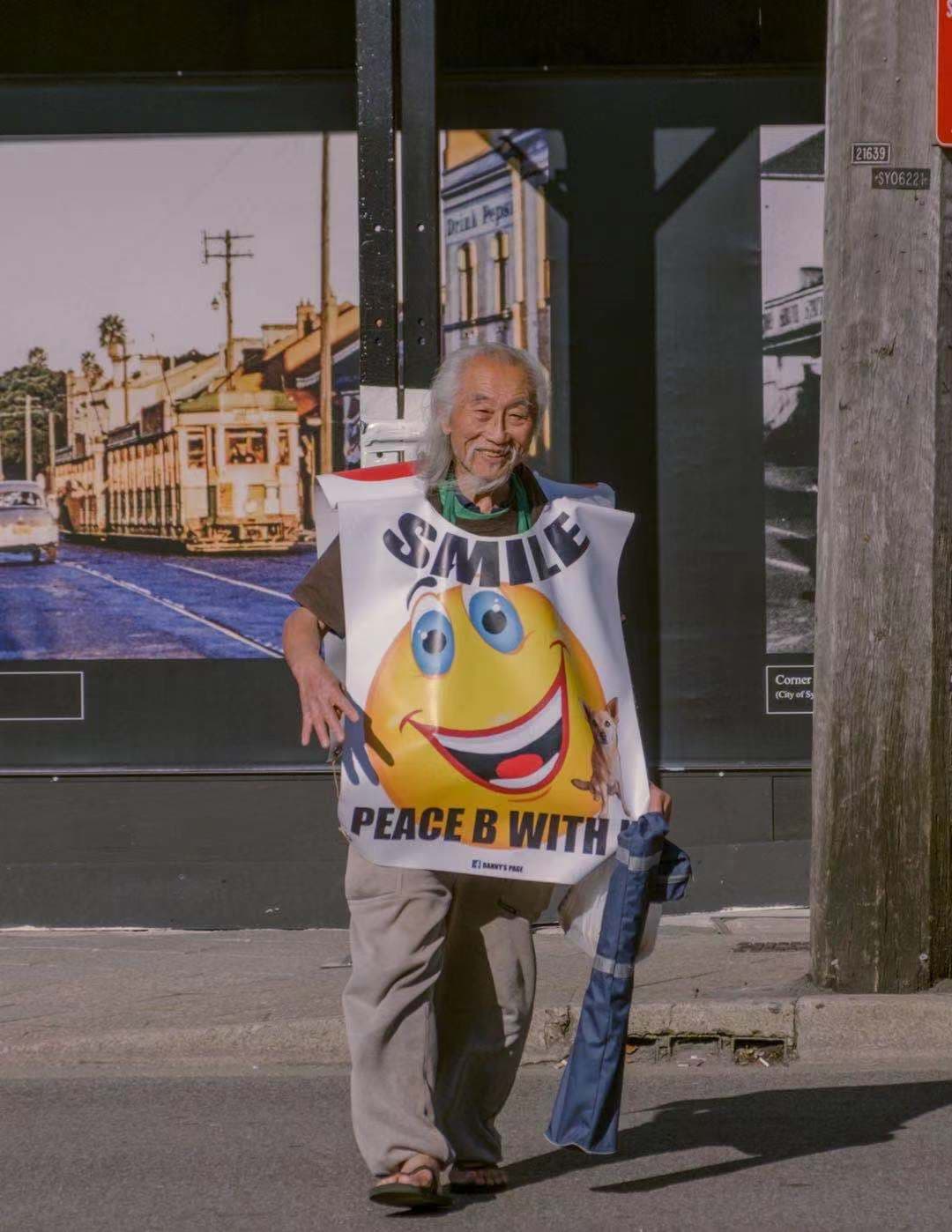 an old man with a smiley face sign walking towards the camera