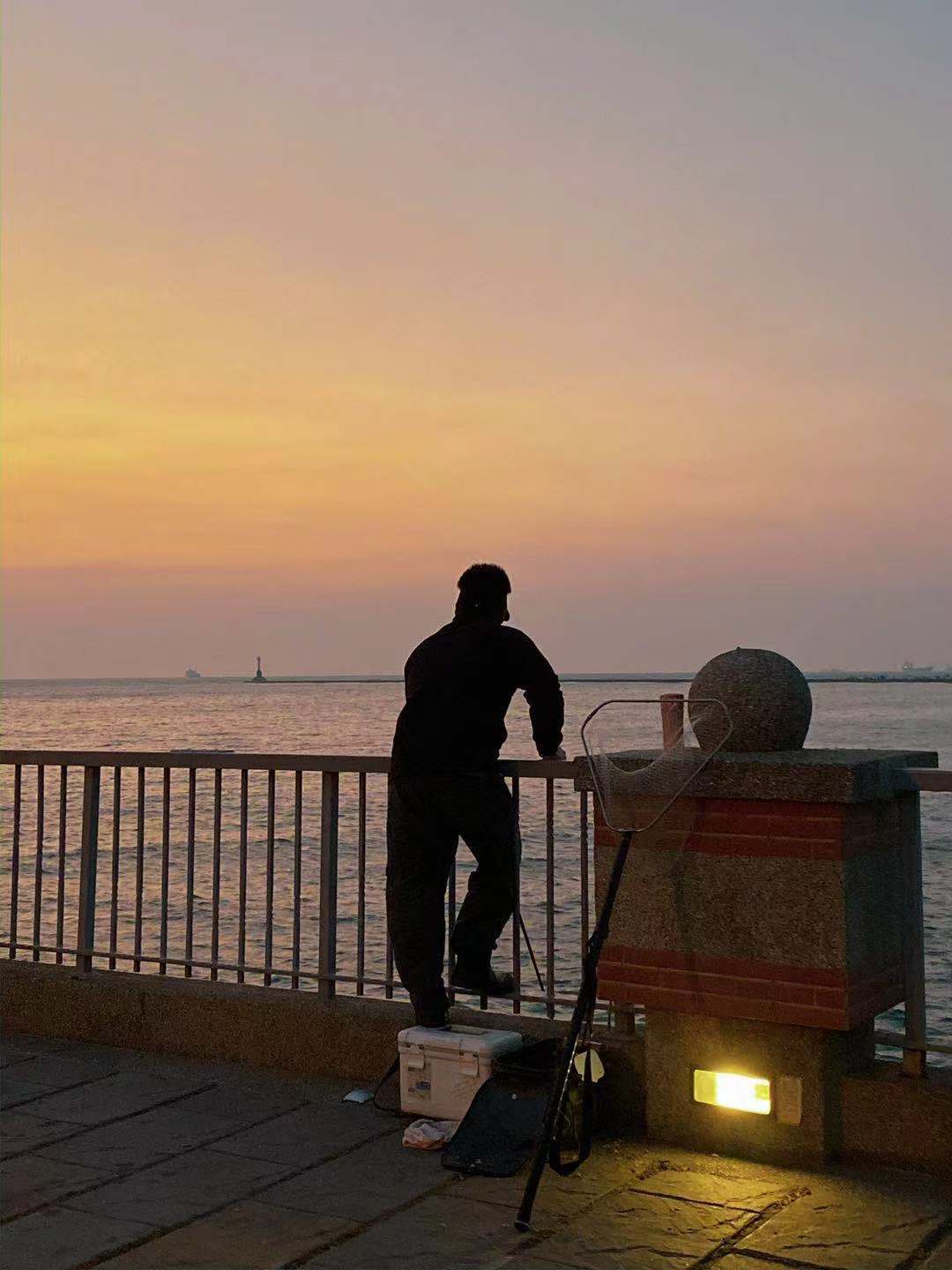 A back view of a man near a lake viewing an orange sunset