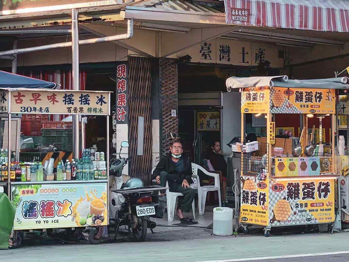 A far view of a middle aged man sitting in front of an old store